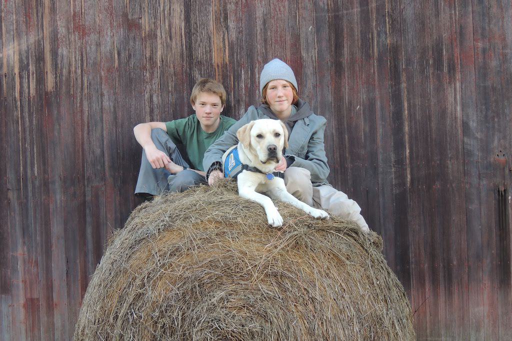 Rowan, Gabe, and yellow lab Nacho pose on top of a hay bale. 