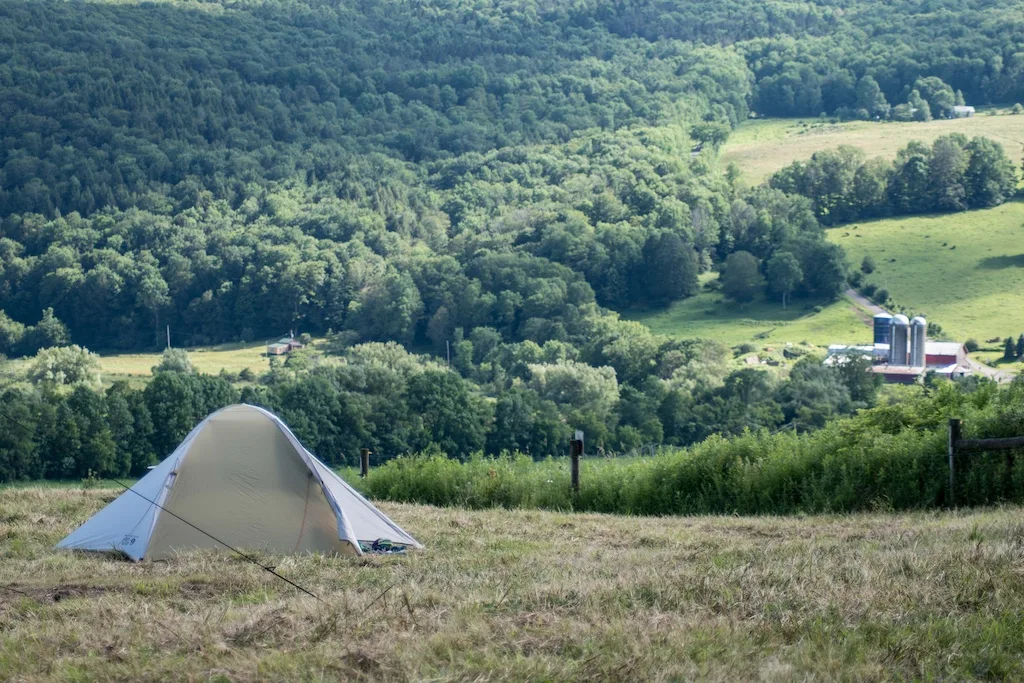 A tent on a hillside overlooking a farm in New York. 